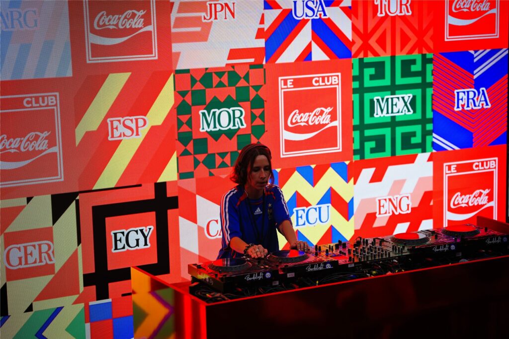 DJ devant l'écran aux couleurs des nations du Mondial 2026 au Club Coca-Cola