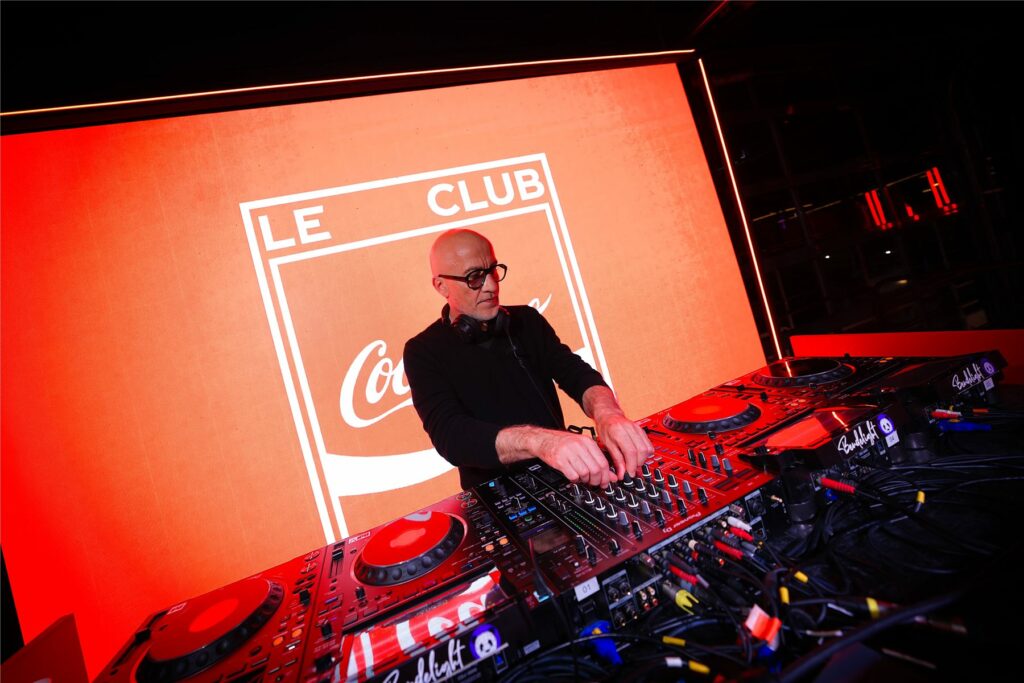 DJ aux platines devant l'écran Le Club Coca-Cola en soirée