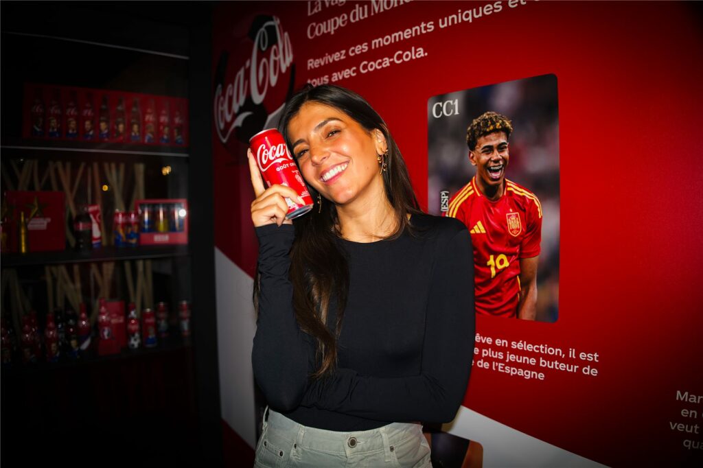 Une invitée tient une canette Coca-Cola devant un visuel de footballeur de l'équipe d'Espagne