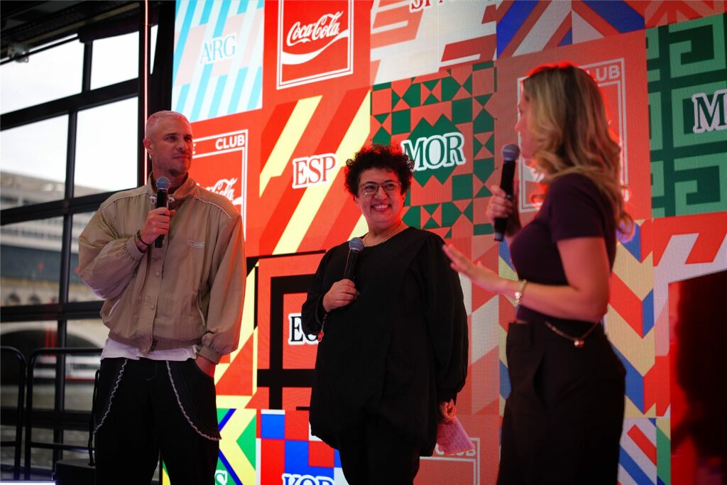 Trois intervenants sur scène devant l'écran du Club Coca-Cola pendant la soirée