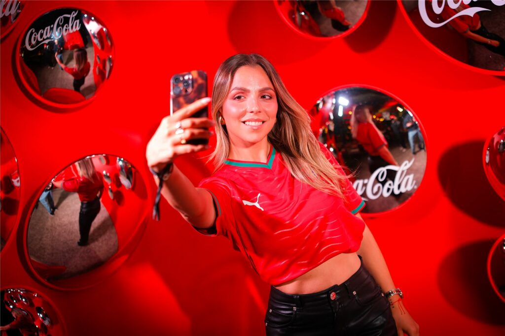 Une invitée prend un selfie devant le mur de miroirs Coca-Cola