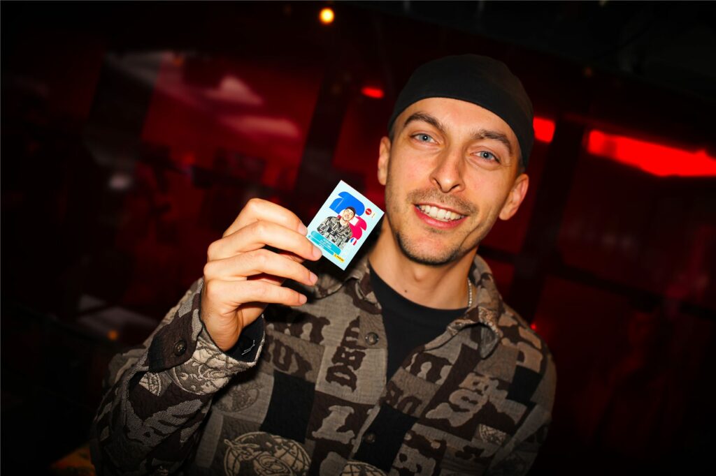 Un invité montre son sticker Panini personnalisé au Club Coca-Cola