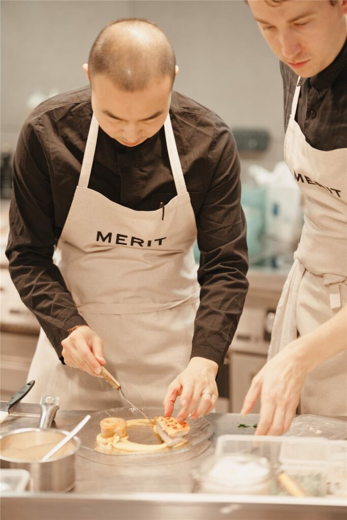Deux chefs en tablier Merit dressant les assiettes en cuisine