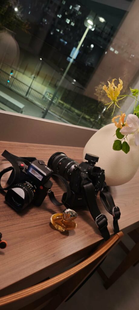 Coulisses : deux appareils photo posés près d'un flacon New Wave et d'un bouquet