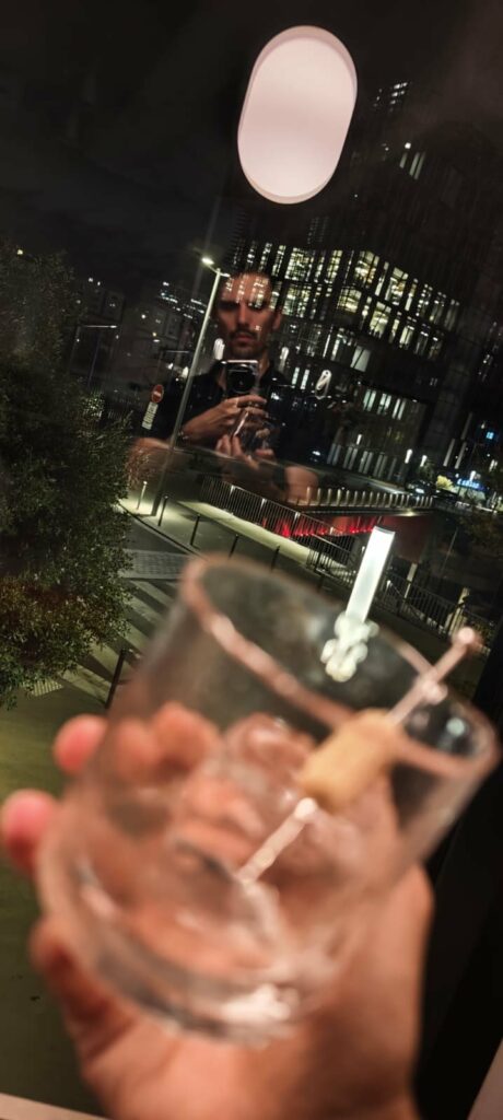 Coulisses : reflet du photographe dans la vitre, verre à la main, Paris de nuit