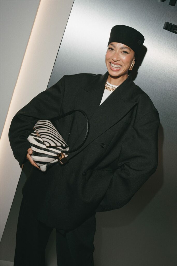 Invitée souriante en manteau noir et chapeau, sac zébré à la main