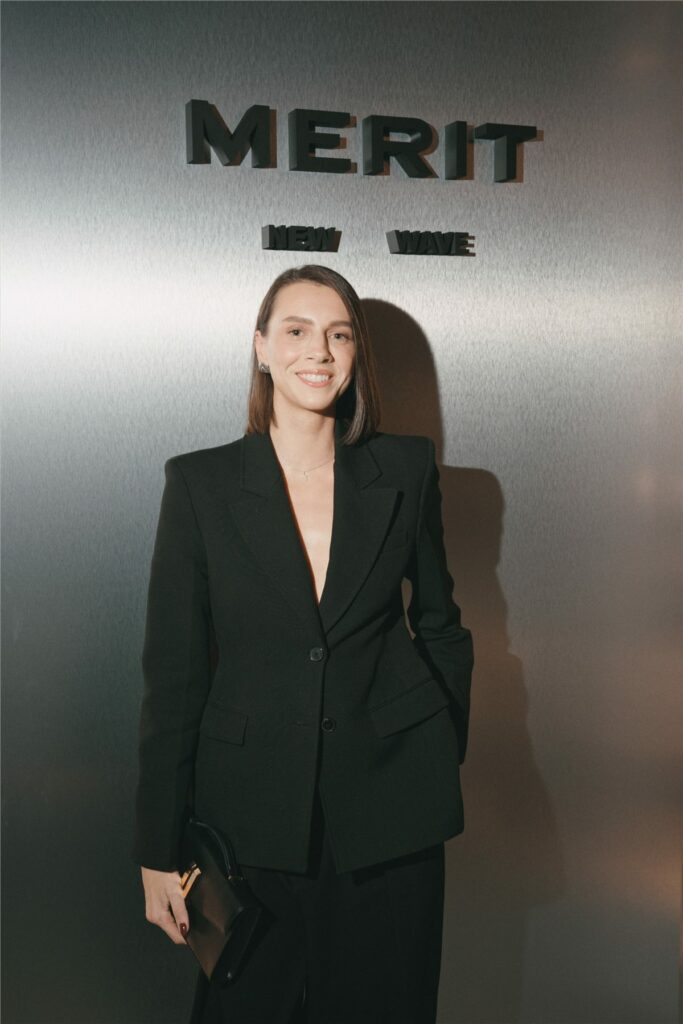 Invitée en tailleur noir devant le mur au logo Merit
