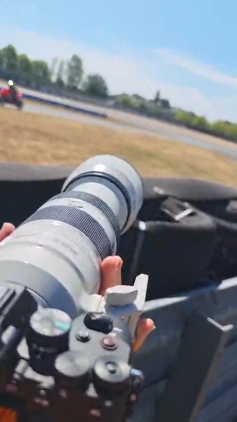 Coulisses : appareil photo et téléobjectif au bord de la piste du Circuit Carole, avec une moto au loin