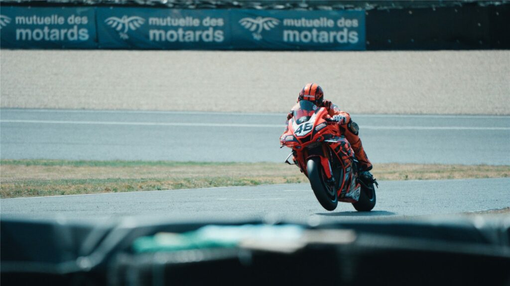 Moto orange très inclinée en virage devant le muret du Circuit Carole
