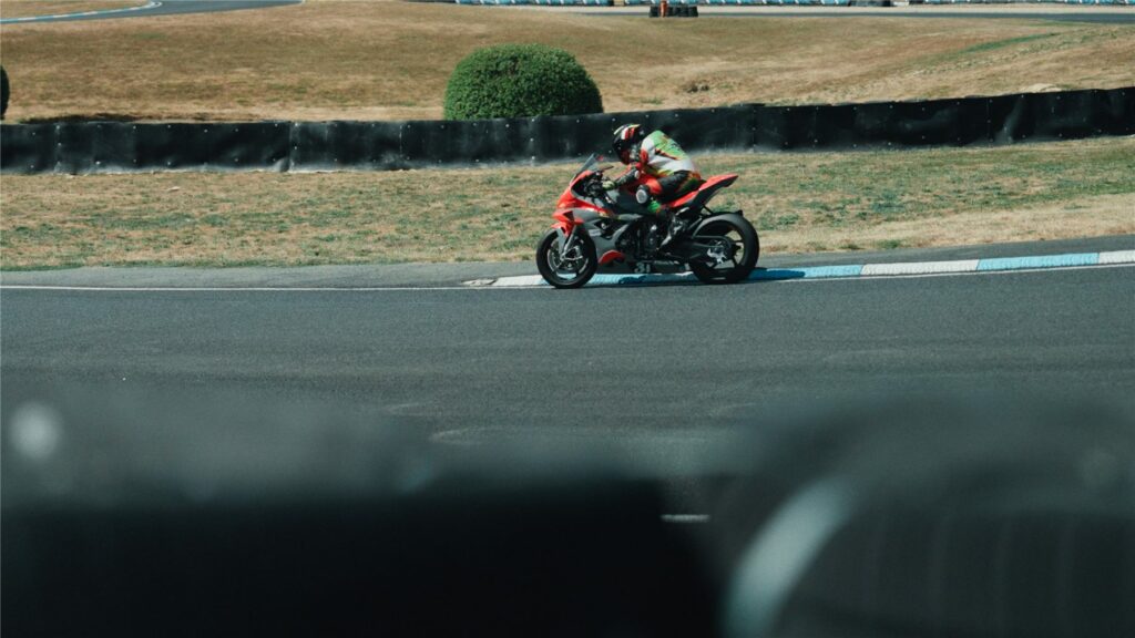 Moto rouge et noire en courbe sur le Circuit Carole avec des pneus au premier plan