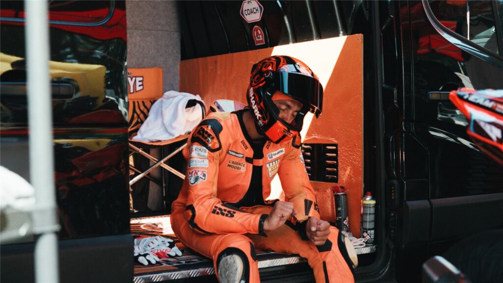 Geoffroy Dehaye casque sur la tête, assis dans le stand en combinaison orange