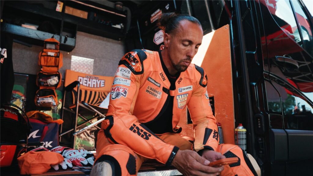 Geoffroy Dehaye assis en combinaison orange dans son stand, concentré avant la session