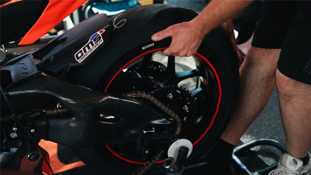 Mécanicien tenant la roue arrière d'une moto de course orange et noire