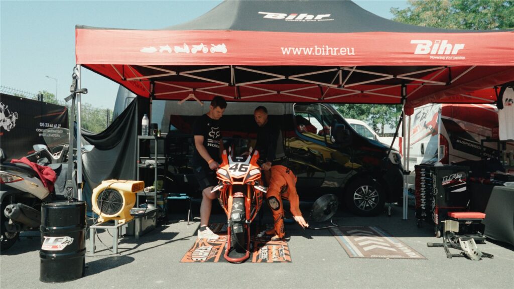 Stand de l'équipe sous une tente rouge avec la moto orange de Geoffroy Dehaye et ses mécaniciens